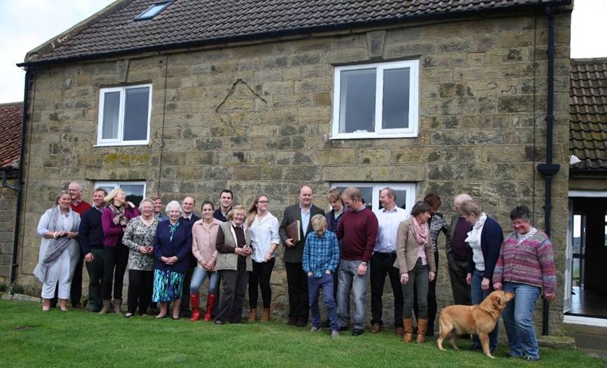 A group of people standing in front of a stone building
Description automatically generated